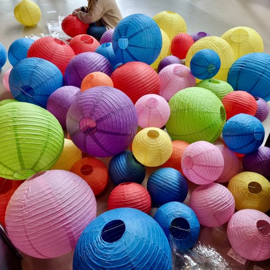 Veel gekleurde papieren lampionnen in diverse kleuren op de grond.