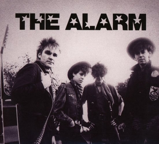 De band The Alarm staat in een zwart-witfoto met vier leden. Een gitarist staat links.