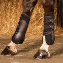Zwarte paardenbeschermers om de benen van een paard, opgesteld op hooi.