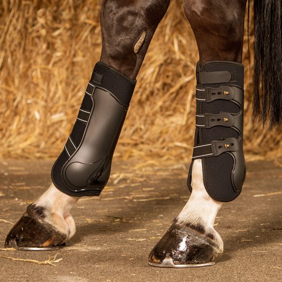 Zwarte paardenbeschermers om de benen van een paard, opgesteld op hooi.