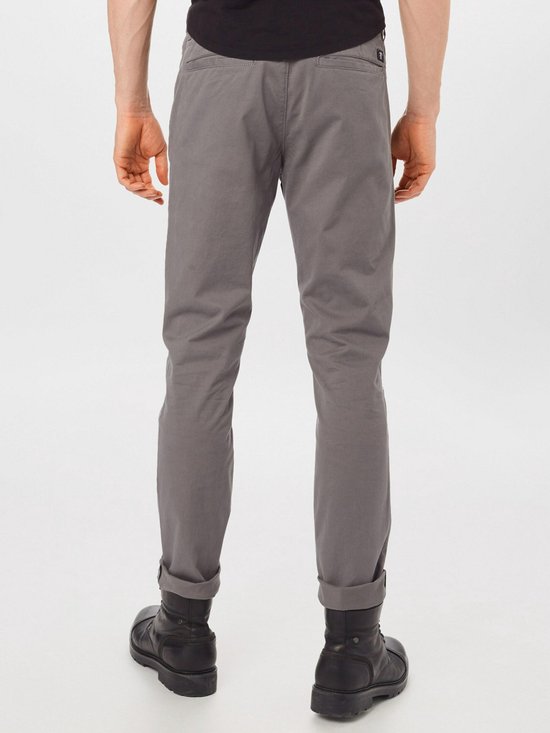 Achterkant van grijze chino broek met omgeslagen broekspijpen en zwarte laarzen.
