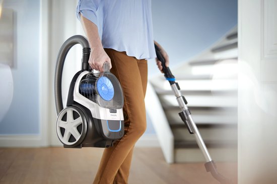 Femme portant un aspirateur blanc avec des accents bleus près d'un escalier.