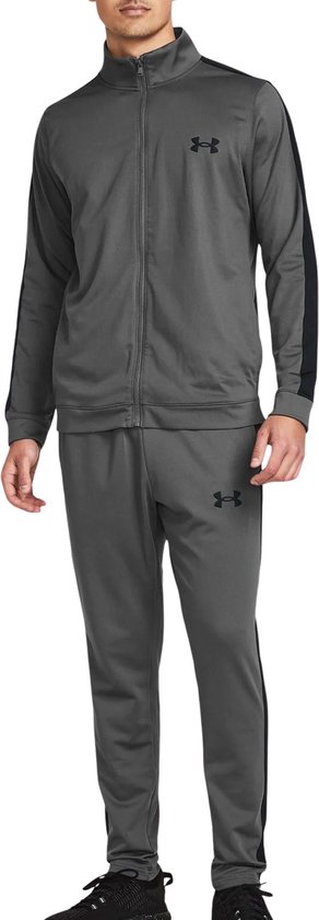 Man met grijze trainingsset: jack met zwarte strepen en logo, en broek met zwarte strepen en logo.
