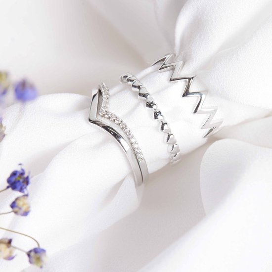 Twee zilveren ringen op witte stof: een V-vormige ring met zirkonia en een ring met hartjes.