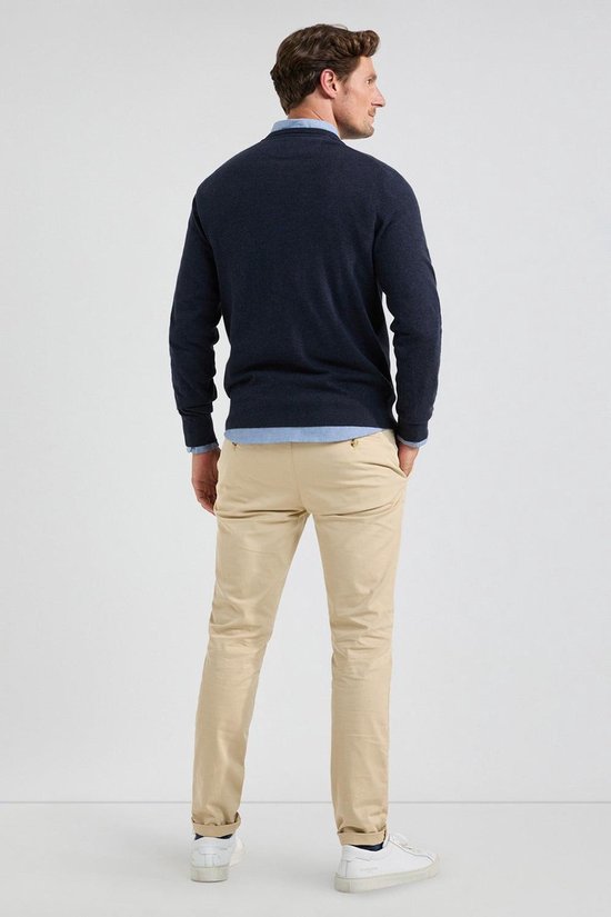 Achterkant van een man die een marineblauwe V-hals trui draagt met een lichtblauw overhemd en beige broek.