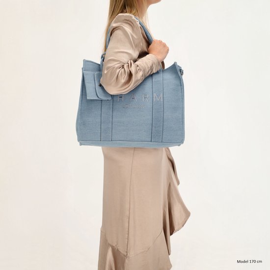 Model van 170 cm draagt een lichtblauwe denim shopper met 'CHARM LONDON' opdruk en een klepje.