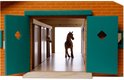 Gezicht op een houten paardenstal met rode bakstenen façade, groene deuren open, bruin paard in hal.
