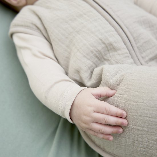Detail van babyhandje op een beige babyslaapzak.