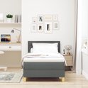 Donkergrijze boxspring opgemaakt met wit beddengoed, staand in een opgeruimde slaapkamer met bureau.