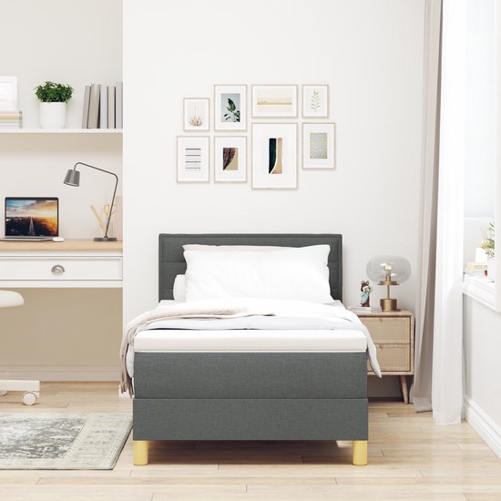 Donkergrijze boxspring opgemaakt met wit beddengoed, staand in een opgeruimde slaapkamer met bureau.