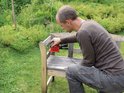 Man schuurt een houten bankje in de tuin met een rode Einhell multischuurmachine.