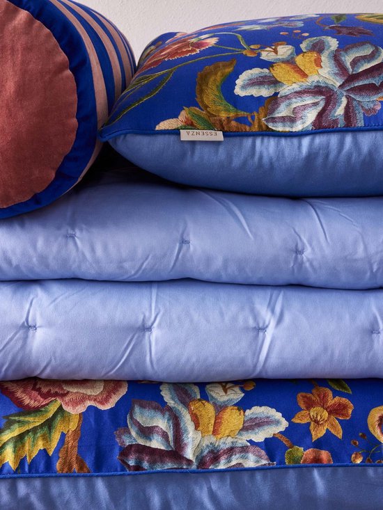 Gestapelde kussens: een blauw kussen met bloemenprint, een lichtblauw gewatteerd dekbed en nog een blauw kussen met bloemenprint.