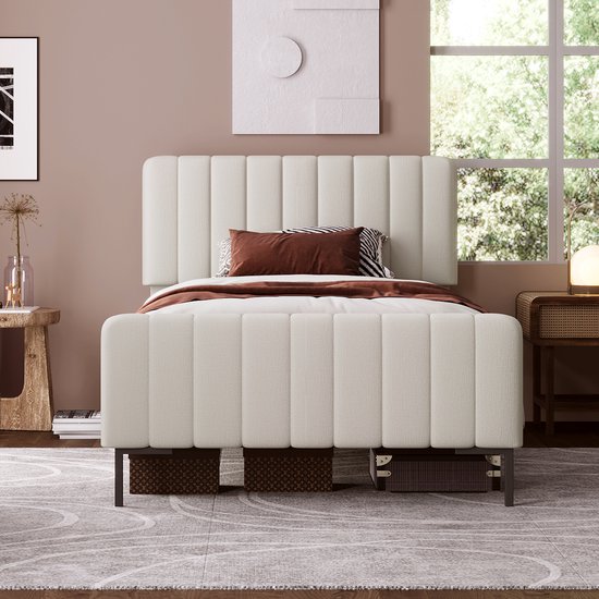 Un lit rembourré beige clair avec des détails rayés, décoré de coussins marron et à rayures noires et blanches.