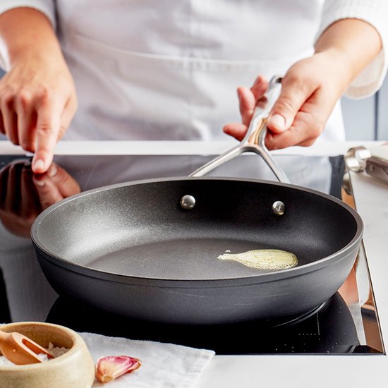 Een chef-kok met witte schort bereidt vis in een zwarte koekenpan met een metalen handgreep. Boter sist in de pan.