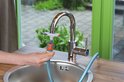 Hand bevestigt een oranje en grijze tuinslangadapter aan een zilverkleurige kraan.