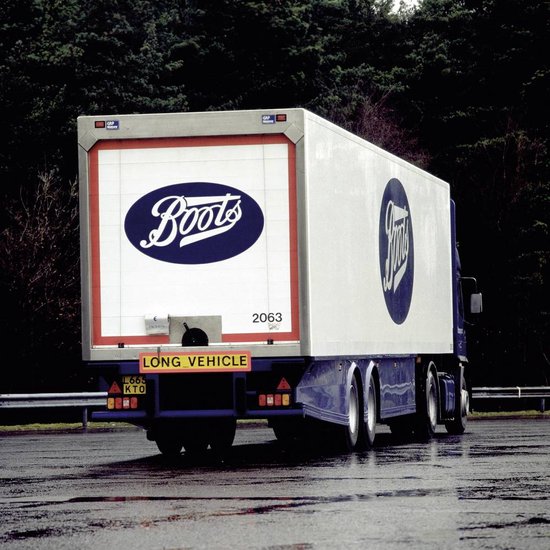 Witte vrachtwagen met blauwe 'Boots'-logo's, 'LONG VEHICLE'-bord, rode rand, kenteken L665 KTO.