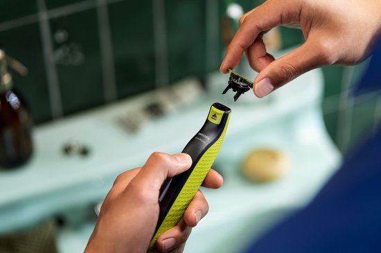 Hand houdt zwarte en felgroene OneBlade scheerapparaat vast. Vingers bevestigen een kamstuk op de scheerkop.