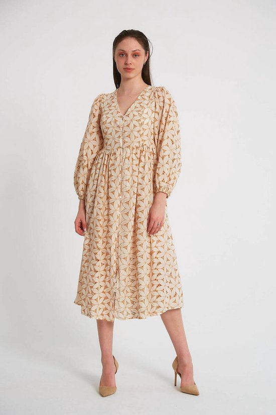 Model in crèmekleurige jurk met lange pofmouwen en camel geometrisch patroon, op hoge hakken.