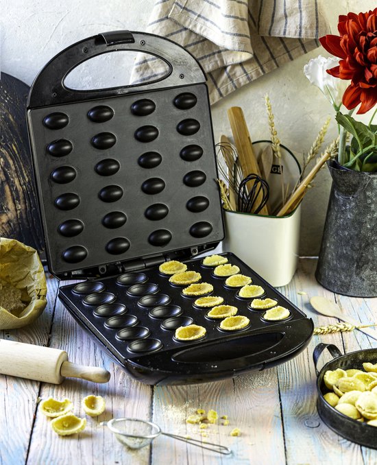 Zwarte koekjesmaker geopend, met de eerste laag nootjeskoekjes erin, op een houten tafel.