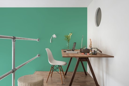 Een bureau met een witte stoel, laptop en bloemen op een groene muur.