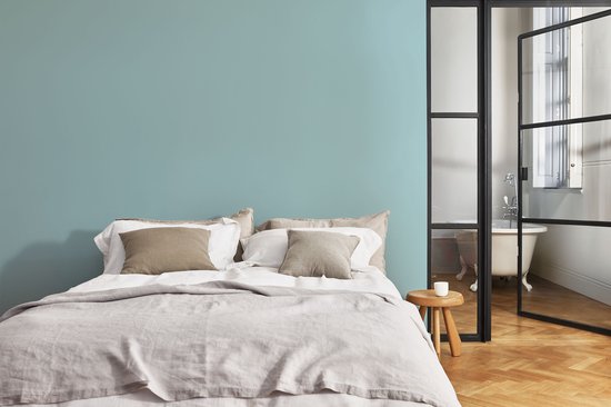Slaapkamer met lichtblauwe muur, bed met linnen en een open badkamer.