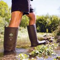 Man in bruine Muck Boot Wetland Pro laarzen loopt door ondiep water.