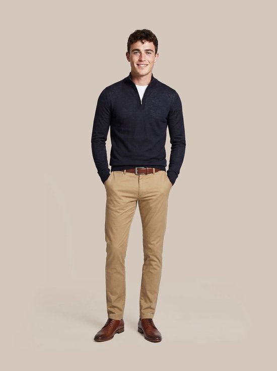 Man met donkerblauwe trui met rits, witte t-shirt en lichtbruine chino broek.
