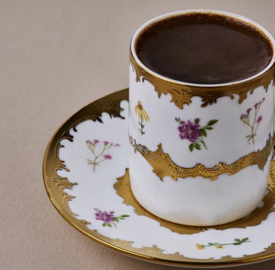 Close-up van een wit porseleinen koffiekopje gevuld met koffie, versierd met bloemen en gouden details.