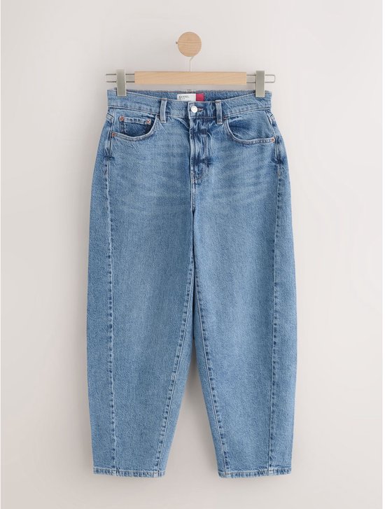 Blauwe jeans met wijde, ronde pijpen hangend aan een kledinghanger.