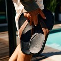 Man houdt bruine leren Reef slippers met zwarte zolen vast.