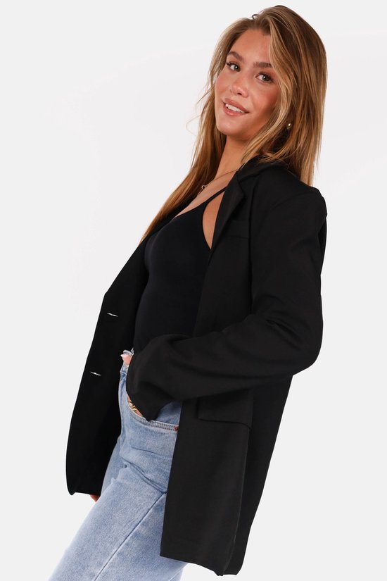 Mannequin aux longs cheveux blonds, portant un blazer noir avec un top noir et un jean bleu clair.