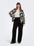 Model draagt een zwarte broek met wijde pijpen en een beige top, gecombineerd met een bomberjack met zwart-witte zebraprint.