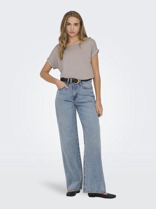Model met een lichtbruine top met omgeslagen korte mouwen, wijde jeans en een zwarte riem.