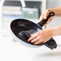 Handen die een lichtblauwe pan met zwarte binnenkant en grijze greep afdrogen.
