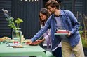 Een man en vrouw die samen gerechten van een buitentafel pakken, met stapels kommen en schalen.