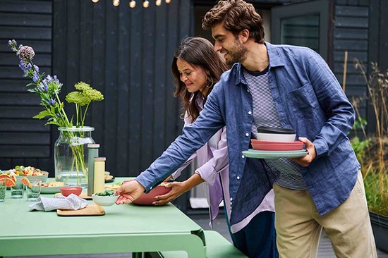 Een man en vrouw die samen gerechten van een buitentafel pakken, met stapels kommen en schalen.