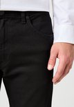 Close-up van de voorkant van een zwarte Wrangler jeans, met een hand in de zak.