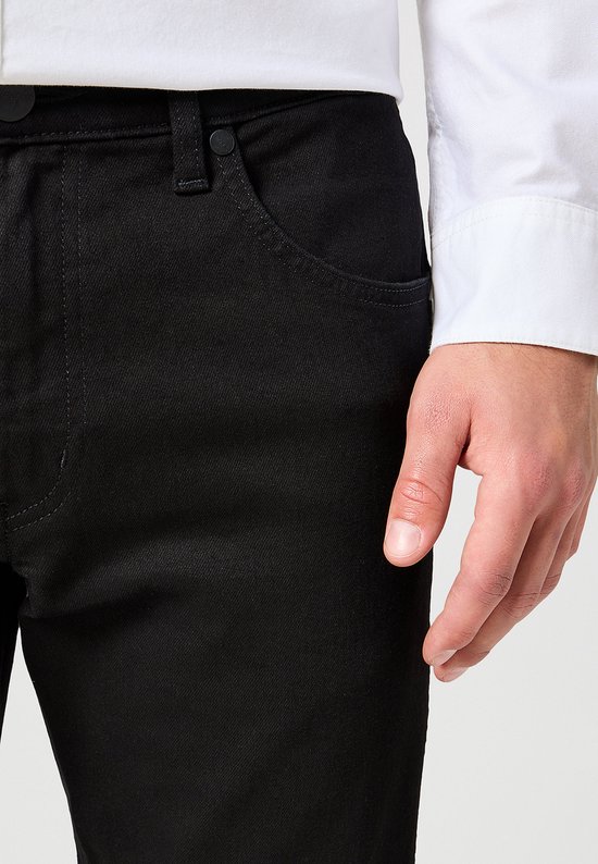 Close-up van de voorkant van een zwarte Wrangler jeans, met een hand in de zak.