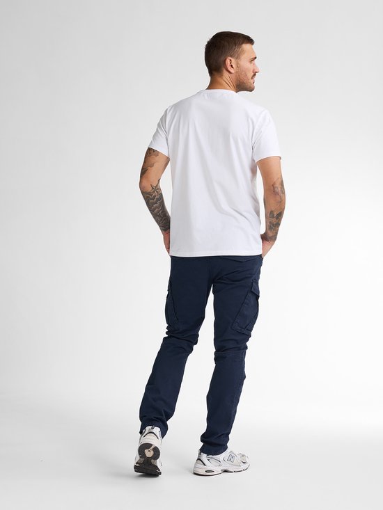 Man met rug naar voren, draagt een witte t-shirt en donkerblauwe cargobroek.