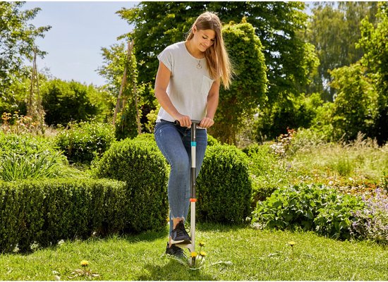 Vrouw met gestreept shirt en jeans onkruid wippend in een tuin met GARDENA onkruidsteker.