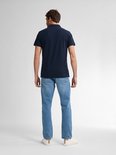 Man in donkerblauw poloshirt en lichtblauwe jeans, staand.