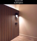 Een zwarte wandlamp op een houten lambrisering, die licht reflecteert op de muur.