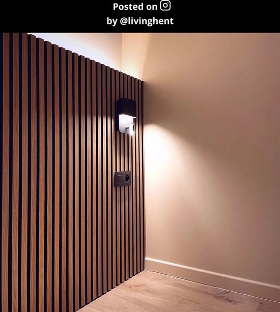 Een zwarte wandlamp op een houten lambrisering, die licht reflecteert op de muur.