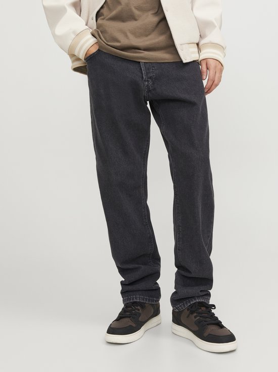 Benen van een man in een bruin T-shirt, grijze spijkerbroek en bruine sneakers.