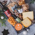 Een open borrelbox met diverse kazen, worst, crackers, chips, noten, saus en wijn.