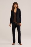 Model draagt zwarte blazer met bruine kanten top en zwarte broek.