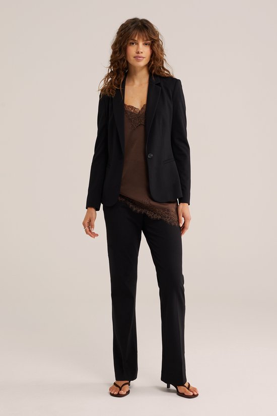 Model draagt zwarte blazer met bruine kanten top en zwarte broek.
