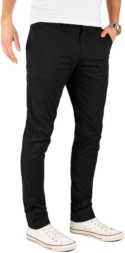 Zij-aanzicht van een man in een zwarte slim fit chinobroek, witte t-shirt en witte sneakers. De hand van de man zit in zijn zak.