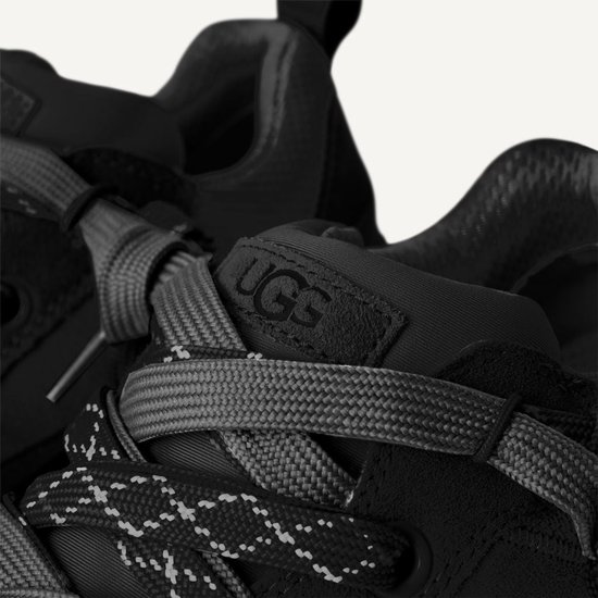 Gedetailleerde opname van de veters en het UGG-logo op een zwarte sneaker.