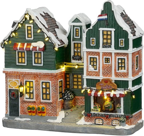 Kerstdorp huisje met rode bakstenen, groene gevels en witte sneeuwbedekte daken. Verlicht met kerstlampjes.